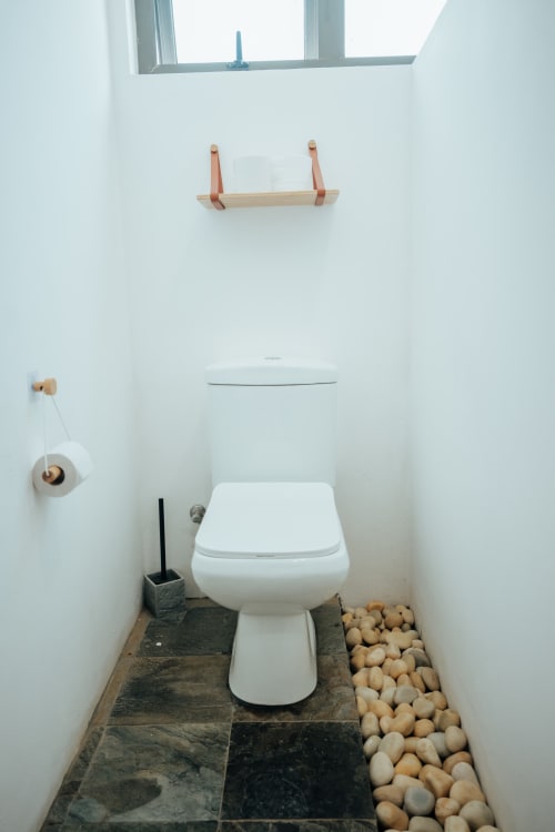 Modern white toilet in villa bathroom at Gerards & Angel, Pereybere with stone tile floor and natural lighting.