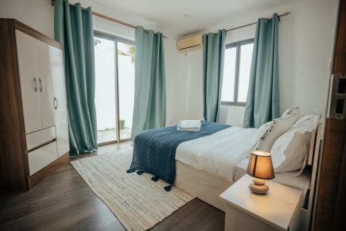 Spacious bedroom at Gerards & Angel villa in Pereybere with queen bed, teal curtains, AC, and pool view access through glass