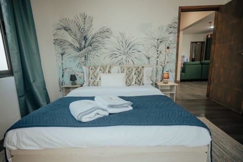 Modern bedroom at Gerards & Angel villa in Pereybere with tropical palm wallpaper, white bed, blue runner, and folded towels