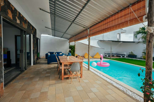 Covered terrace at Gerards & Angel villa in Pereybere with wooden dining table, blue sofa, and turquoise swimming pool with
