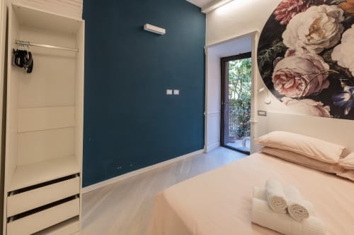 Modern bedroom in Buonanotte Colosseo Rome apartment with teal accent wall, garden view door, and floral artwork