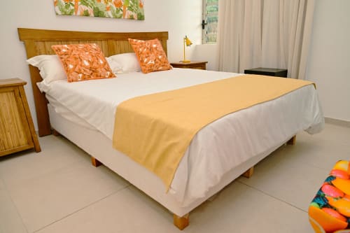 Chambre de l'appartement en bord de mer chez Gerards & Angel avec lit en bois, linge blanc, coussins orange et plaid jaune