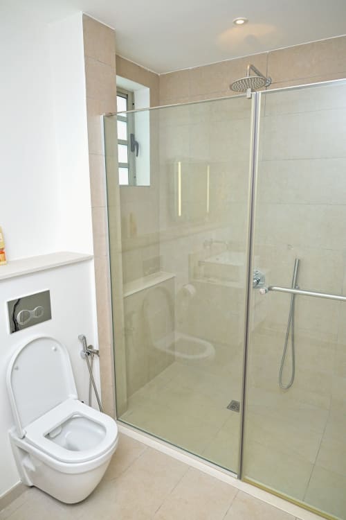 Salle de bain moderne avec toilettes, cabine de douche vitrée et pommeau de douche à effet pluie à l'appartement en bord de mer Gerards & Angel, Pointe