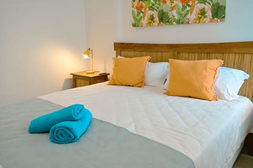 Appartement en bord de mer Gerards & Angel à Pointe aux Piments avec lit fait, lampe jaune, coussins colorés et serviettes roulées