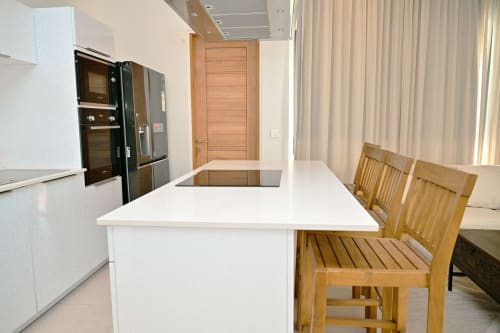 Cuisine moderne avec îlot blanc, électroménagers noirs et chaises en bois dans l'appartement en bord de mer Gerards & Angel, Pointe aux