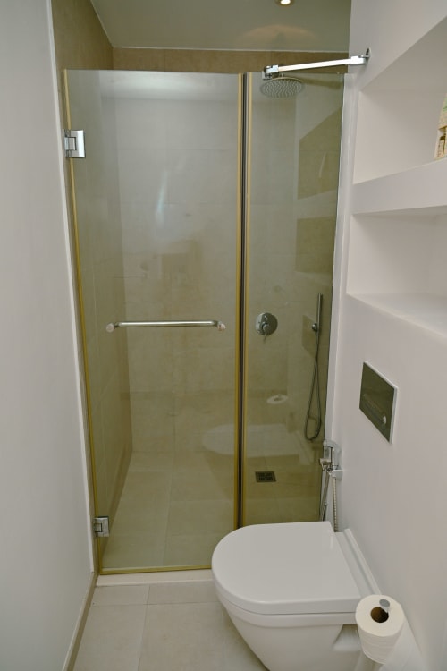 Salle de bain moderne avec douche vitrée, toilettes blanches et carrelage beige de l'appartement en bord de mer Gerards & Angel à Pointe