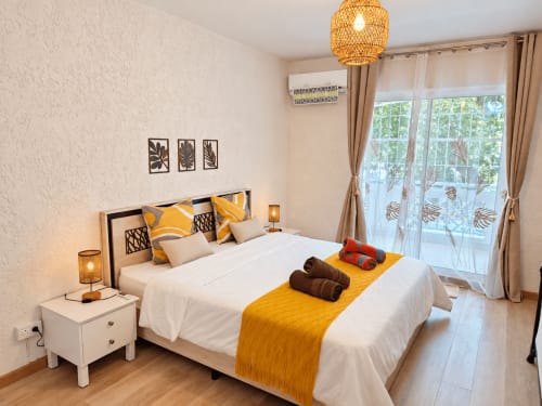 Bright bedroom at Gerards & Angel in Flic-en-Flac with yellow accents, white bed, woven pendant lamp, and balcony overlooking
