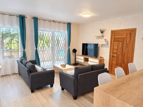 Modern living room with gray sofas, wooden TV stand, and blue curtains at Ti Palmier apartment, Gerards & Angel, Flic-en-Flac