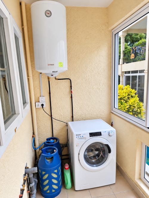 Utility room in Ti Palmier apartment at Gerards & Angel, Flic-en-Flac, with washing machine, water heater, and garden view