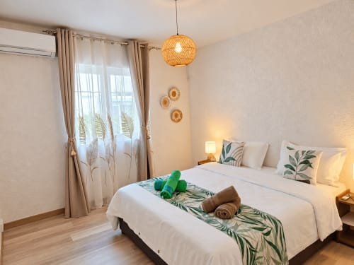 Tropical bedroom at Gerards & Angel in Flic-en-Flac with woven pendant light, plant-patterned curtains, and pool-view balcony