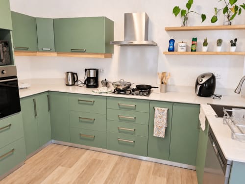 Modern green and white kitchen with stainless steel appliances, wooden shelves with plants, and white countertops at Gerards