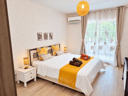 Bright bedroom at Gerards & Angel with yellow accents, white bedding, tropical décor, and pool-view balcony in Flic-en-Flac