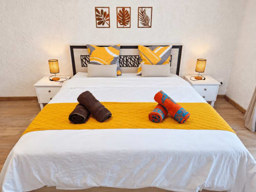 Gerards & Angel Ti Palmier bedroom with yellow accents, rolled towels, and tropical leaf wall decor in Flic-en-Flac