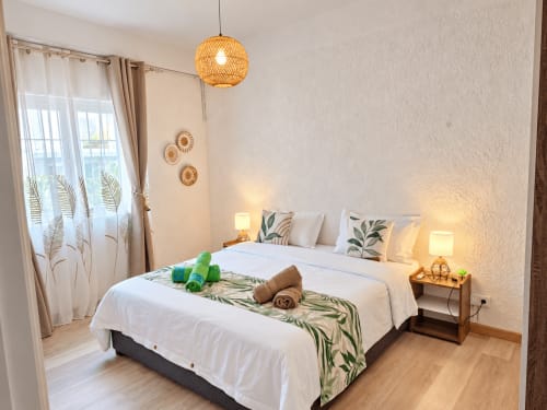 Bright bedroom at Gerards & Angel with queen bed, woven pendant lamp, decorative baskets, and tropical plant motifs in
