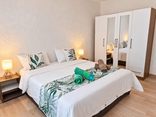 Modern bedroom at Gerards & Angel, Flic-en-Flac with white bedding, tropical decor, mirrored wardrobe, and bedside lamps
