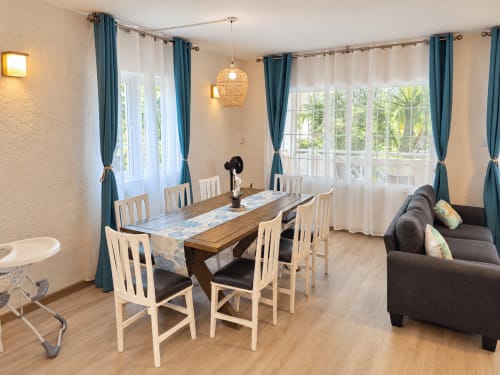 Modern dining area in Ti Palmier apartment at Gerards & Angel, Flic-en-Flac, with wooden table, white chairs, and garden