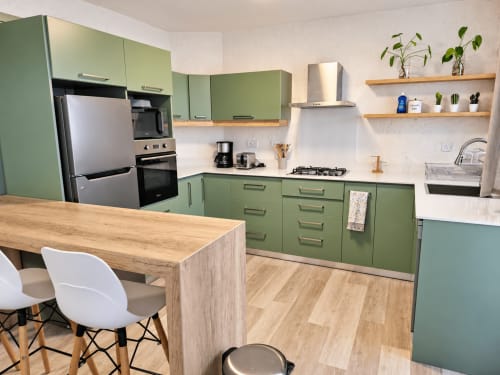Modern kitchen with sage green cabinets, wooden countertop island, stainless steel appliances, and potted plants on shelves