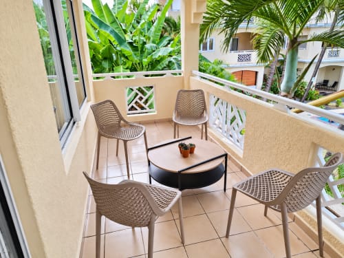 Balcony seating area at Ti Palmier apartment in Flic-en-Flac with modern chairs, coffee table, and tropical garden views