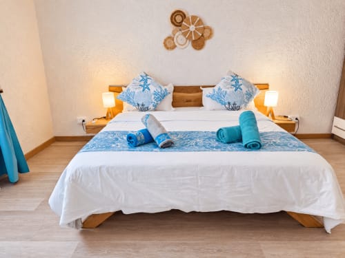 Tropical bedroom at Gerards & Angel, Flic-en-Flac with blue starfish pillows, rolled towels, wooden bed frame, and