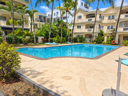 Bright blue rectangular pool surrounded by sand, lounge chairs, and palm trees at Gerards & Angel hotel in Flic-en-Flac,