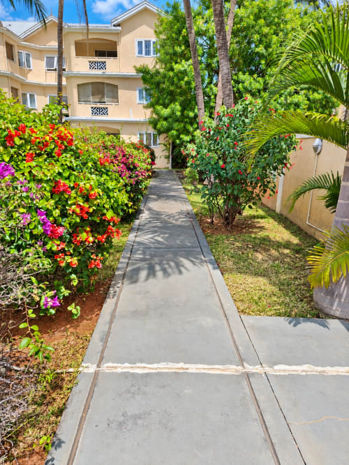 Colorful flower-lined walkway leading to beige apartment building at Gerards & Angel in Flic-en-Flac, Mauritius