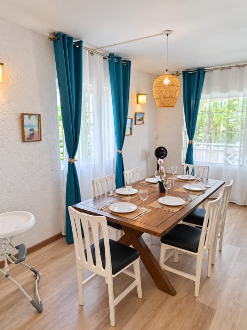 Dining area in Ti Palmier apartment at Gerards & Angel, Flic-en-Flac, with wooden table, cream chairs, and teal curtains