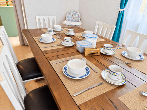 Dining table set for tea service at Gerards & Angel apartment in Flic-en-Flac with white chairs and blue-trimmed dinnerware