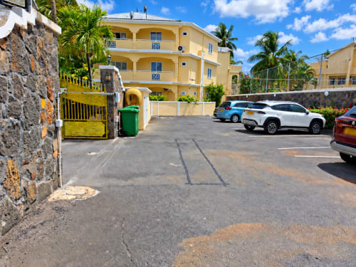 Yellow apartment building with parked cars and palm trees at Gerards & Angel in Flic-en-Flac, Mauritius