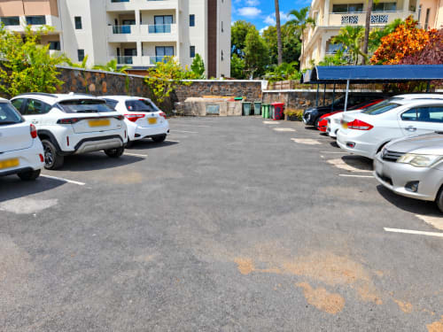 Parking lot at Gerards & Angel hotel in Flic-en-Flac with white cars and colorful tropical gardens nearby