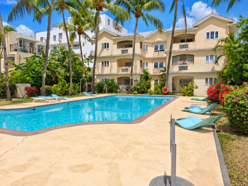 Gerards & Angel pool area in Flic-en-Flac with turquoise swimming pool, lounge chairs, beige apartment building, palm trees,