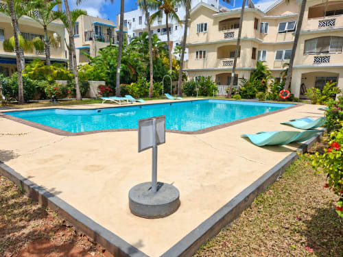 Crystal-blue pool with loungers at Gerards & Angel in Flic-en-Flac, surrounded by palm trees and beige apartments