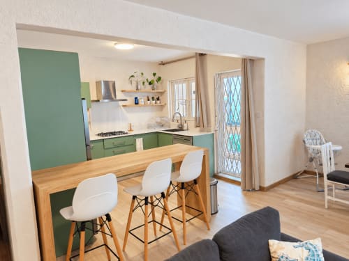 Modern kitchen with green cabinetry, wooden dining table, and white bar stools in Ti Palmier apartment at Gerards & Angel,