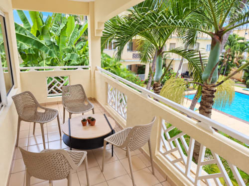 Balcony seating area at Gerards & Angel in Flic-en-Flac with pool view, palm trees, and wicker chairs