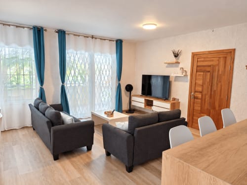 Modern living room at Gerards & Angel with dark sofas, dining table, TV, and balcony view in Flic-en-Flac