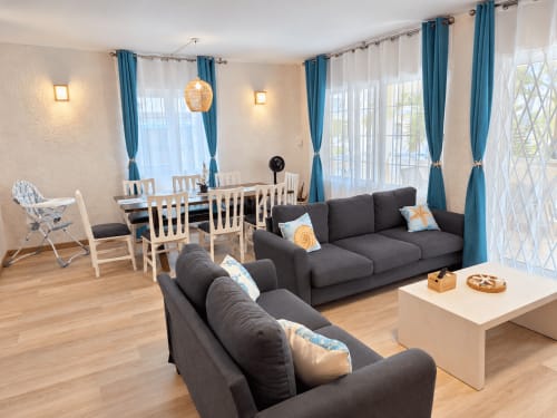 Modern living room at Ti Palmier apartment in Flic-en-Flac with gray sofas, dining area, blue curtains, and garden view