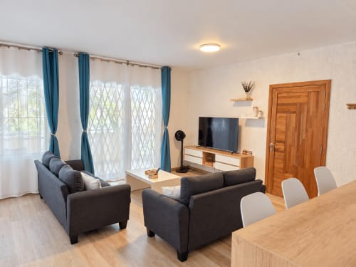 Modern living room at Ti Palmier apartment in Flic-en-Flac with dark sofas, flat-screen TV, wooden furniture, and balcony