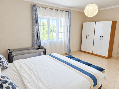 Bright bedroom with queen bed, blue accents, wardrobe, round pendant light, patio doors overlooking garden at Gerards &