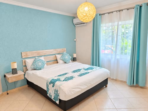 Bright turquoise bedroom at Gerards & Angel, Flic en Flac, with wooden bed, teal cushions, pendant light, and garden view