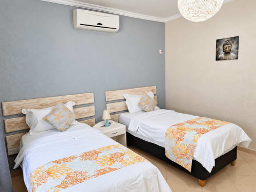 Twin beds with wooden headboards and orange-patterned throws in Sirokann apartment at Gerards & Angel, Flic en Flac