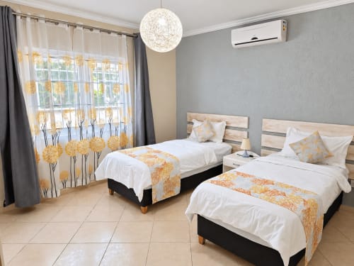 Twin beds with orange floral accents in modern Sirokann apartment at Gerards & Angel, Flic en Flac, featuring AC, string