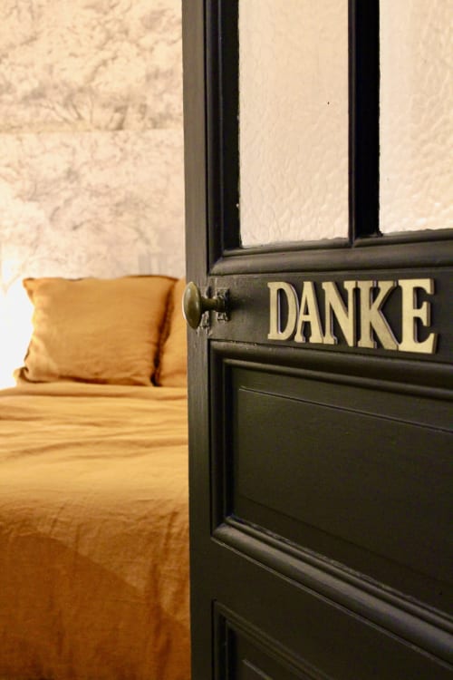 Porte noire avec panneau 'DANKE' ouvrant sur une chambre aux draps dorés à la villa Mi Casa Es Su Casa à Carcassonne