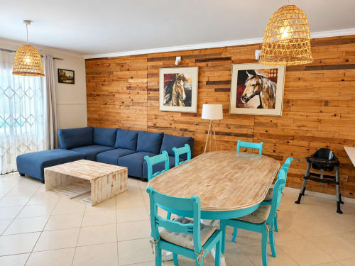 Sirokann apartment living area with blue sofa, turquoise dining chairs, wooden walls, and horse artwork at Gerards & Angel,