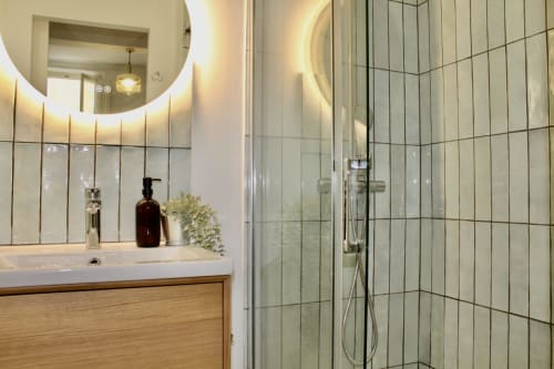 Salle de bain moderne de la villa Mi Casa Es Su Casa à Carcassonne avec miroir rond illuminé, meuble vasque en bois et douche à l'italienne