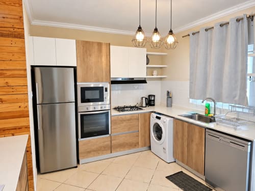 Modern kitchen with stainless steel appliances, wooden cabinetry, washing machine, and pendant lighting at Gerards & Angel