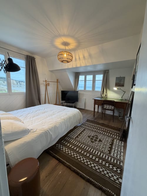 Chambre lumineuse avec vue sur mer au gîte Mon Week End A La Mer, lit blanc, bureau, TV et tapis à motifs