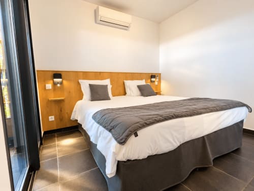 Chambre moderne aux Villas d'A Storia à Zonza avec lit queen-size, tête de lit en bois, draps blancs et vue sur mer