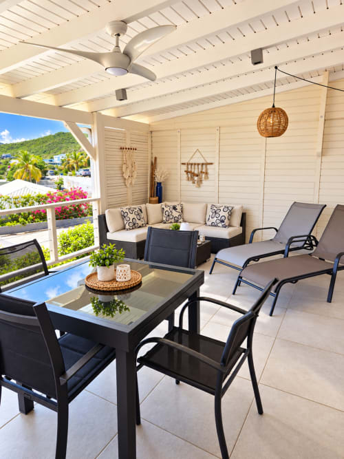 Covered terrace at Les Balcons D'oyster Pond with sea view, featuring black dining table, lounge seating, and ceiling fan in