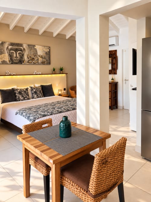 Modern bungalow bedroom in Saint-Martin with bed, wooden desk, wicker chairs, and ocean view access