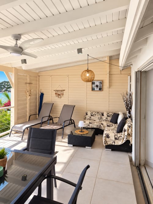 Covered terrace with lounge chairs, patterned sofa, and ceiling fans at Les Balcons D'oyster Pond bungalow in Saint-Martin