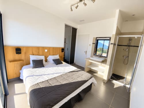Chambre moderne aux Villas d'A Storia, Zonza, avec vue sur mer, tête de lit en bois et salle de bain attenante avec douche